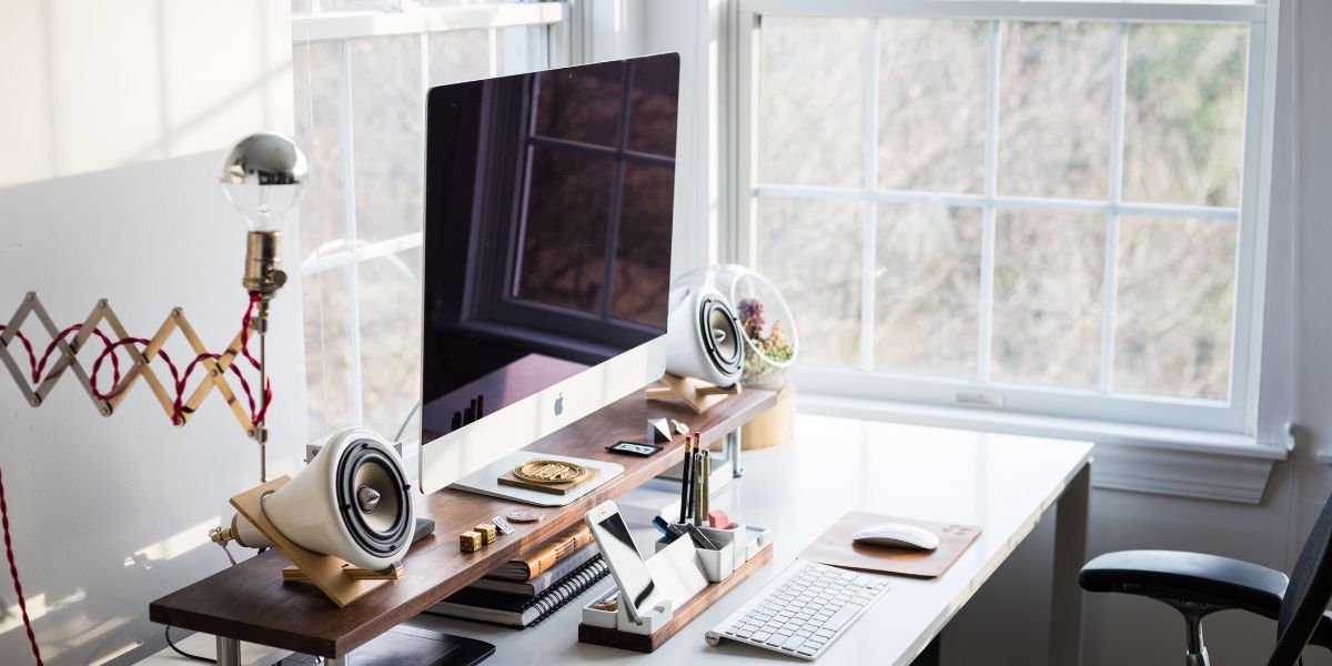 Minimalist home office setup with a large computer, speakers, and desk organizers near a window.